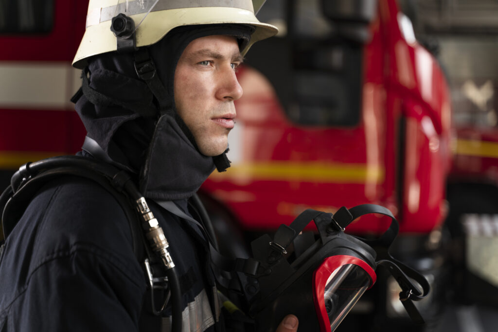 Male firefighter in uniform and helmet standing in a fire station, looking confident.
