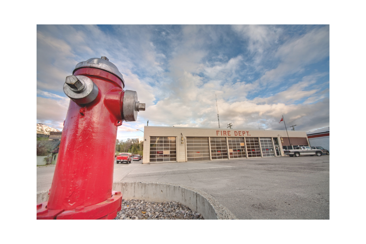 Red fire hydrant in foreground with fire department station in background, highlighting importance of fire hydrant maintenance
