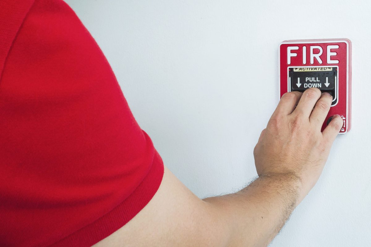 Man reaching out to press a red fire alarm on a wall-mounted hand station. Understanding when a green fire hydrant is used is valuable for maximum efficiency.